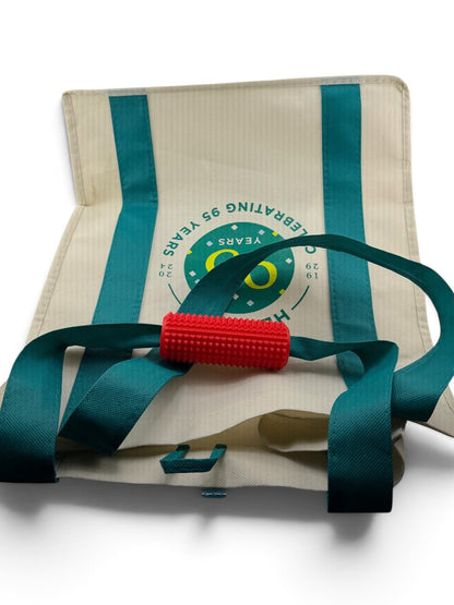 Red Little Ouchies Tag Along sensory fidget clipped onto the strap of a canvas tote bag